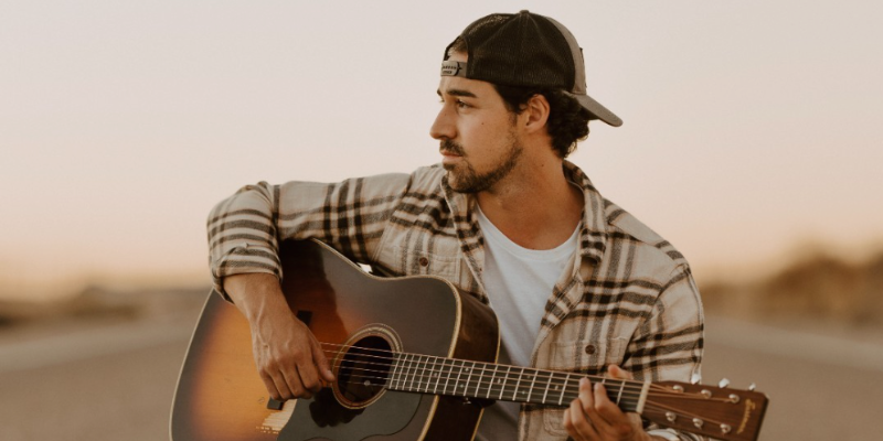 Photo of Jordan Shaw, artist, playing a guitar in a field